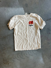 A vintage off-white short-sleeve t-shirt laid flat on a gray concrete floor. The shirt features a small red rectangular graphic on the left chest with the word 'Sedona' printed in black underneath it