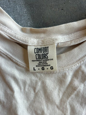Close-up of the inside collar of a cream-colored Comfort Colors t-shirt, showing the brand tag and ribbed neckband on a dark gray textured surface