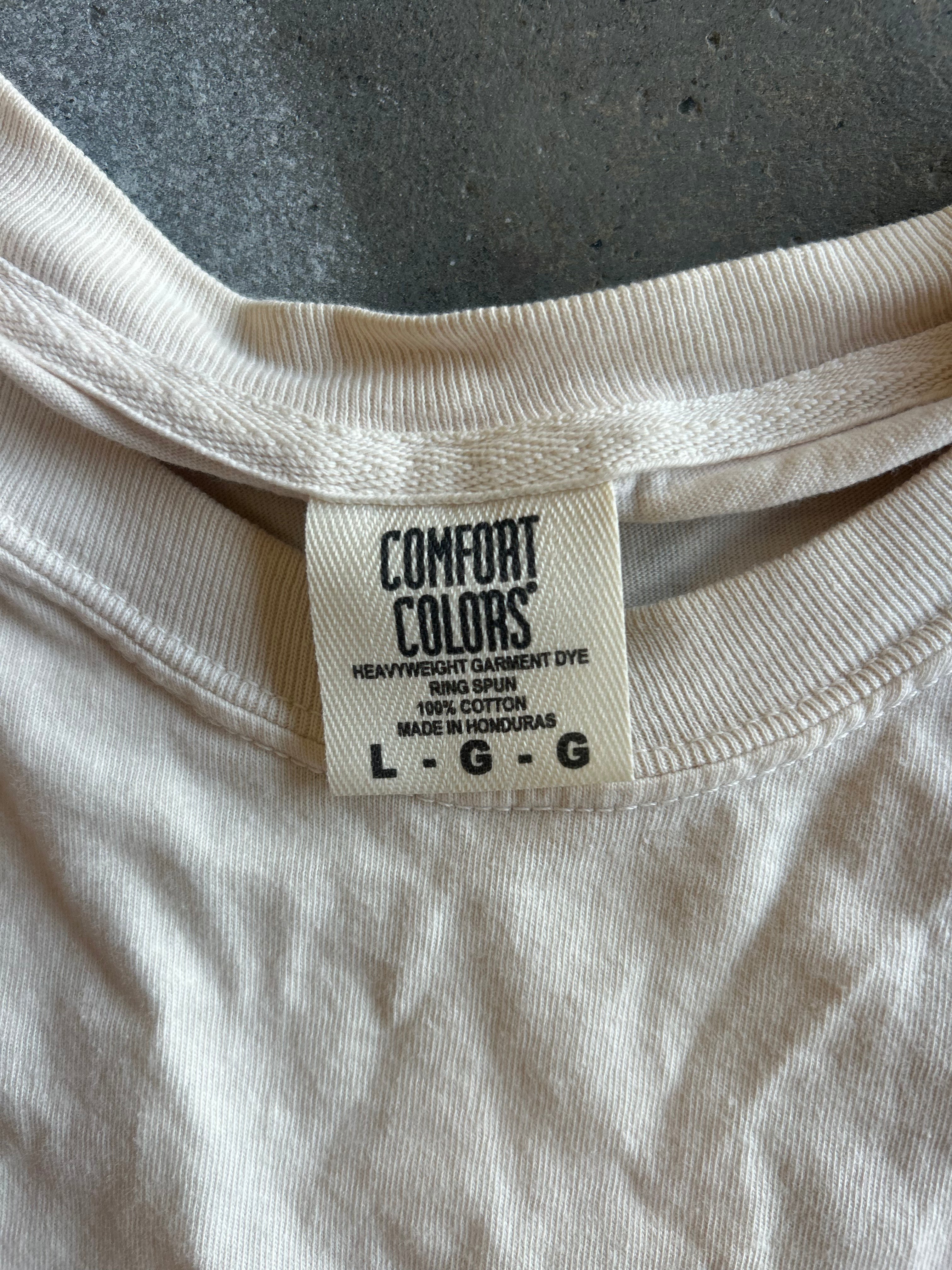 Close-up of the inside collar of a cream-colored Comfort Colors t-shirt, showing the brand tag and ribbed neckband on a dark gray textured surface