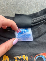 A close-up of a black t-shirt neck label being held by a hand with light pink manicured nails. The label reads '4D THREAD PHIBY-Z' in red and blue