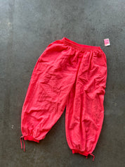 Bright red loose-fitting pants with elastic cuffs and drawstring hems, laid flat on a dark gray concrete surface