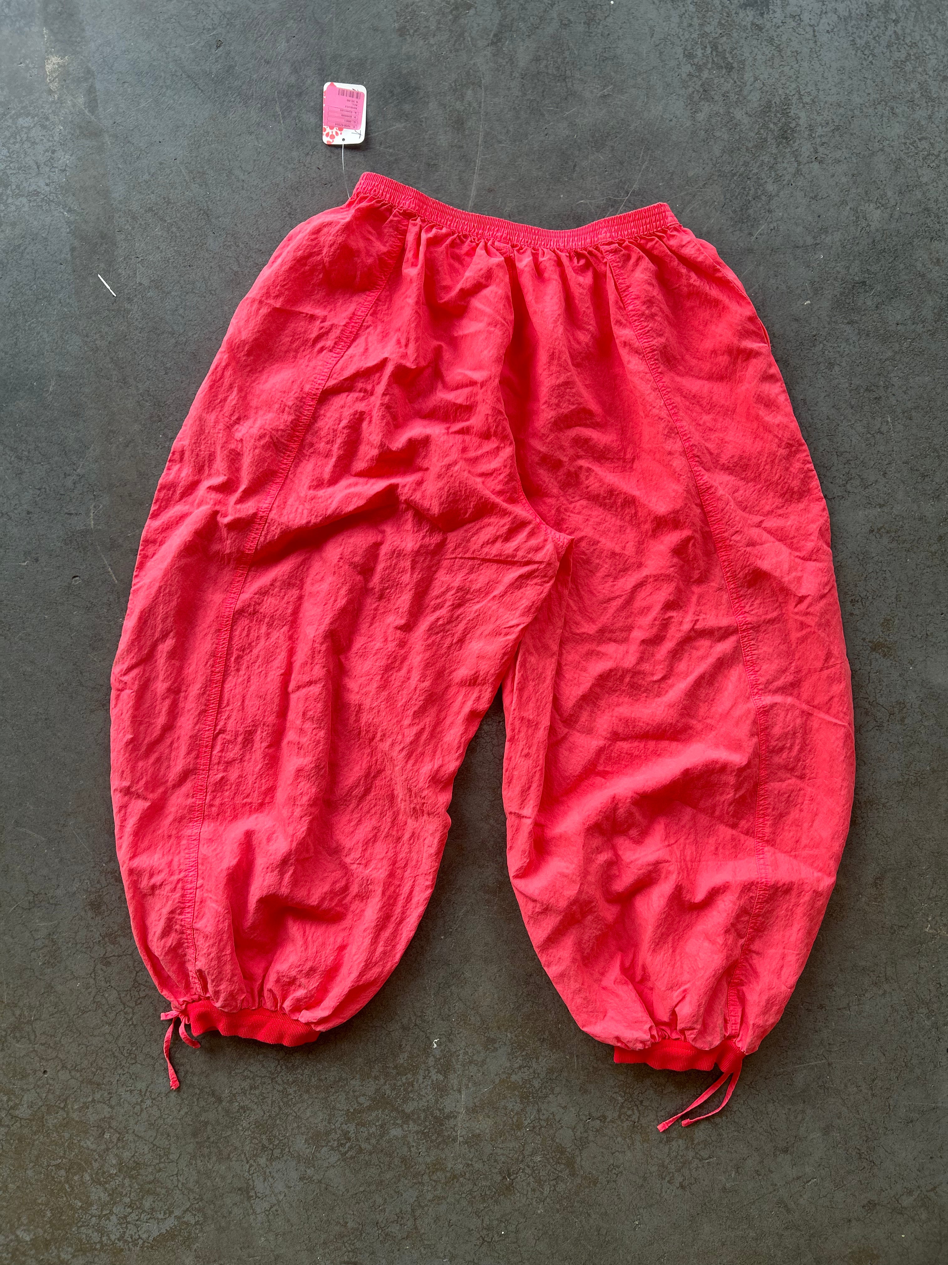 Bright red crinkled cotton harem-style pants with elastic waistband and drawstring ankle cuffs, laid flat on a dark gray textured surface