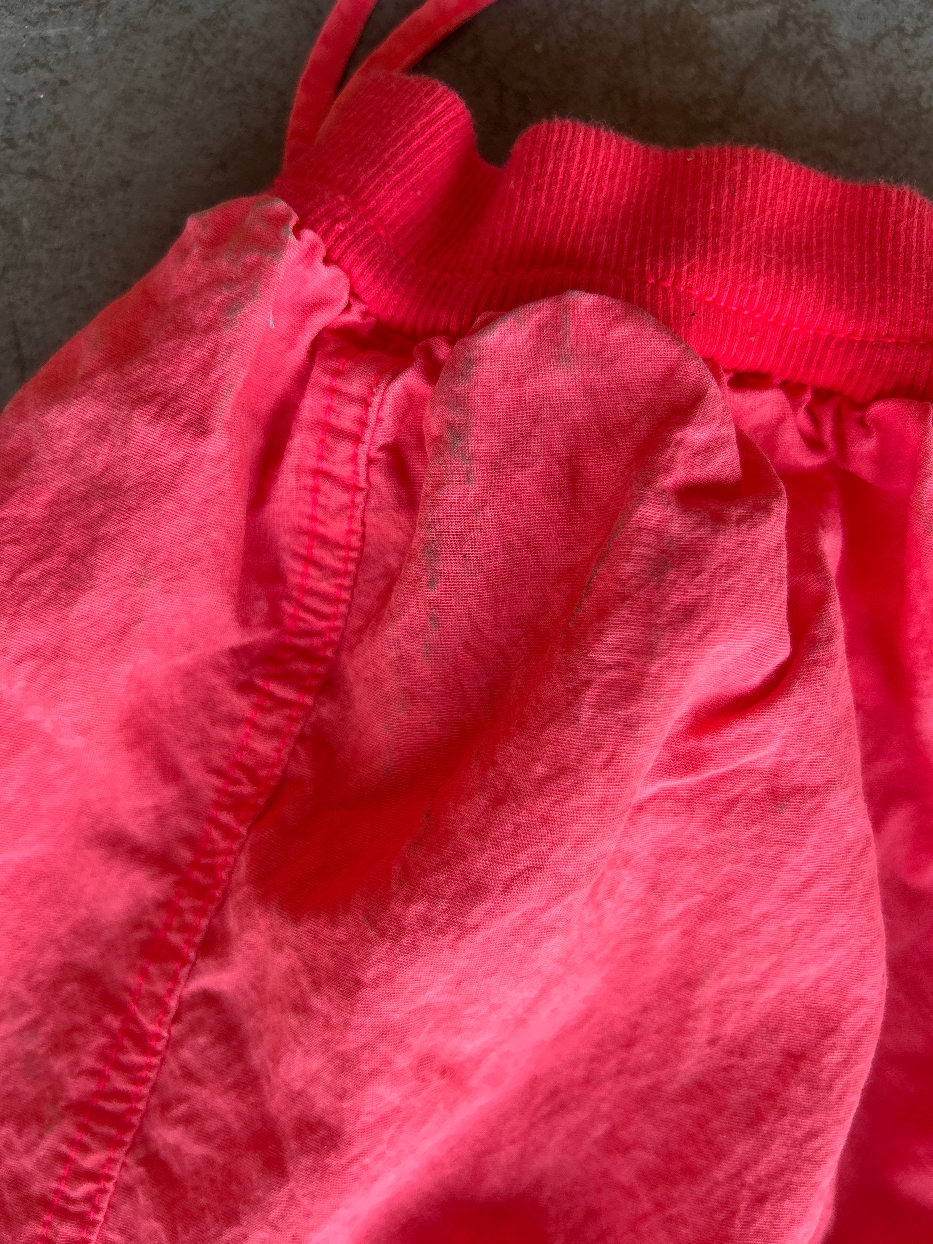 A close-up of a bright pink fabric garment, showing the elastic waistband and gathered material against a dark textured background