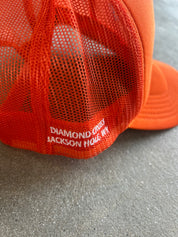 Close-up of an orange trucker hat showing the mesh back and embroidered text 'DIAMOND, OHIO JACKSON HOLE, WY'
