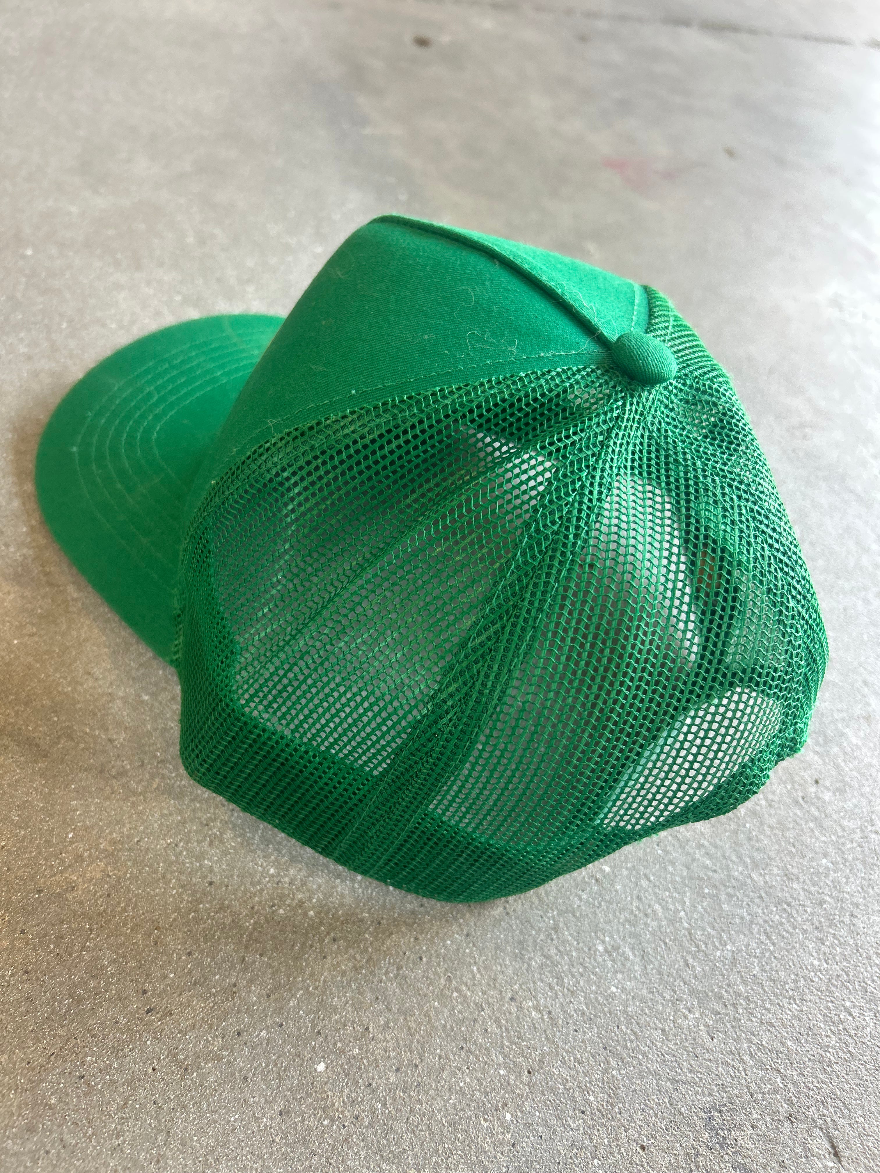 A bright green trucker-style cap with a solid green front panel and green mesh back, photographed on a gray concrete floor