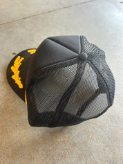 Back of a black mesh trucker hat on a concrete surface