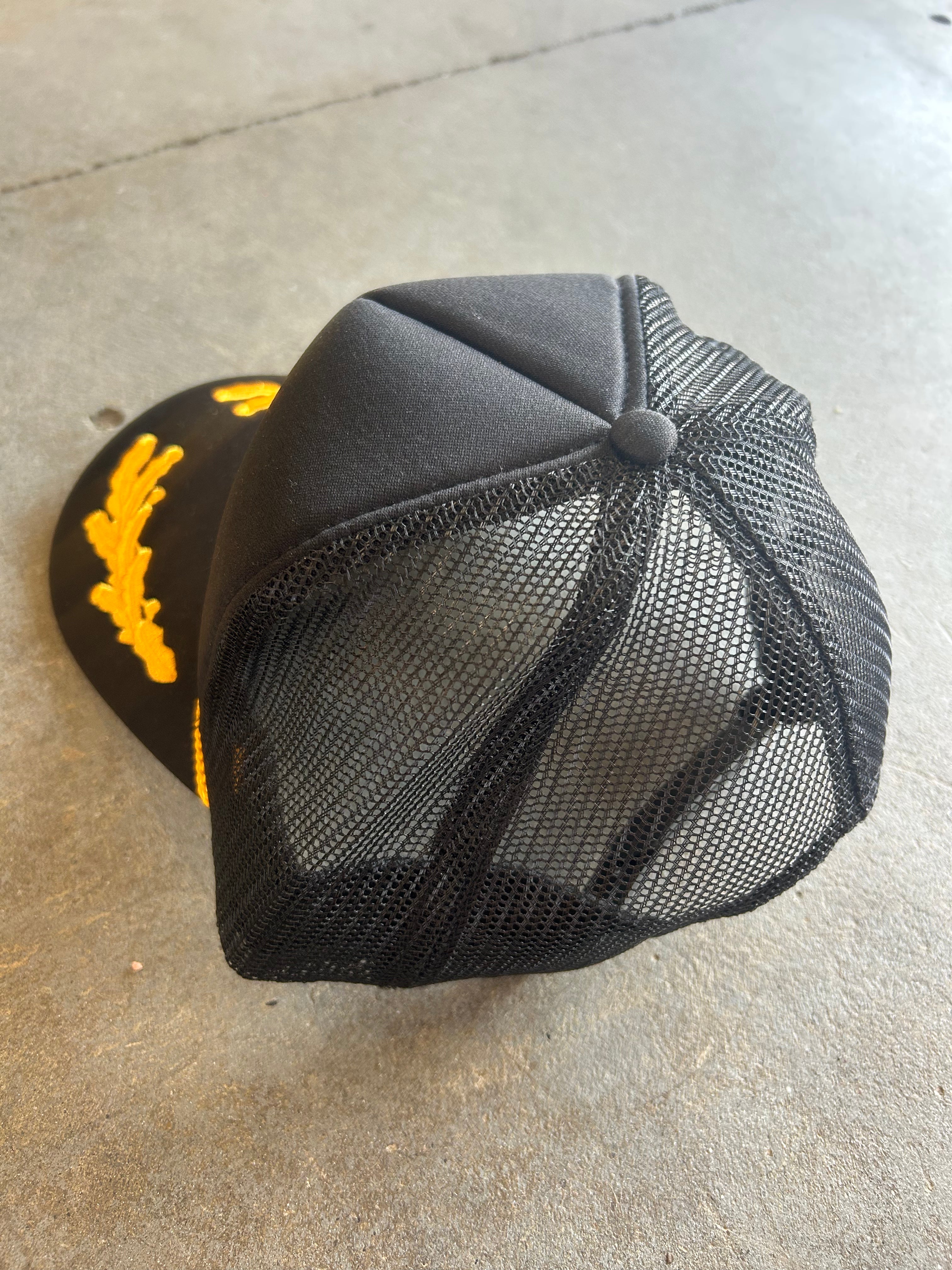 Back of a black mesh trucker hat on a concrete surface