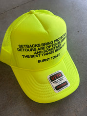 Neon Yellow Trucker Hat with the Burnt Toast theory explanation written in black on the hat, frontal view on a concrete surface