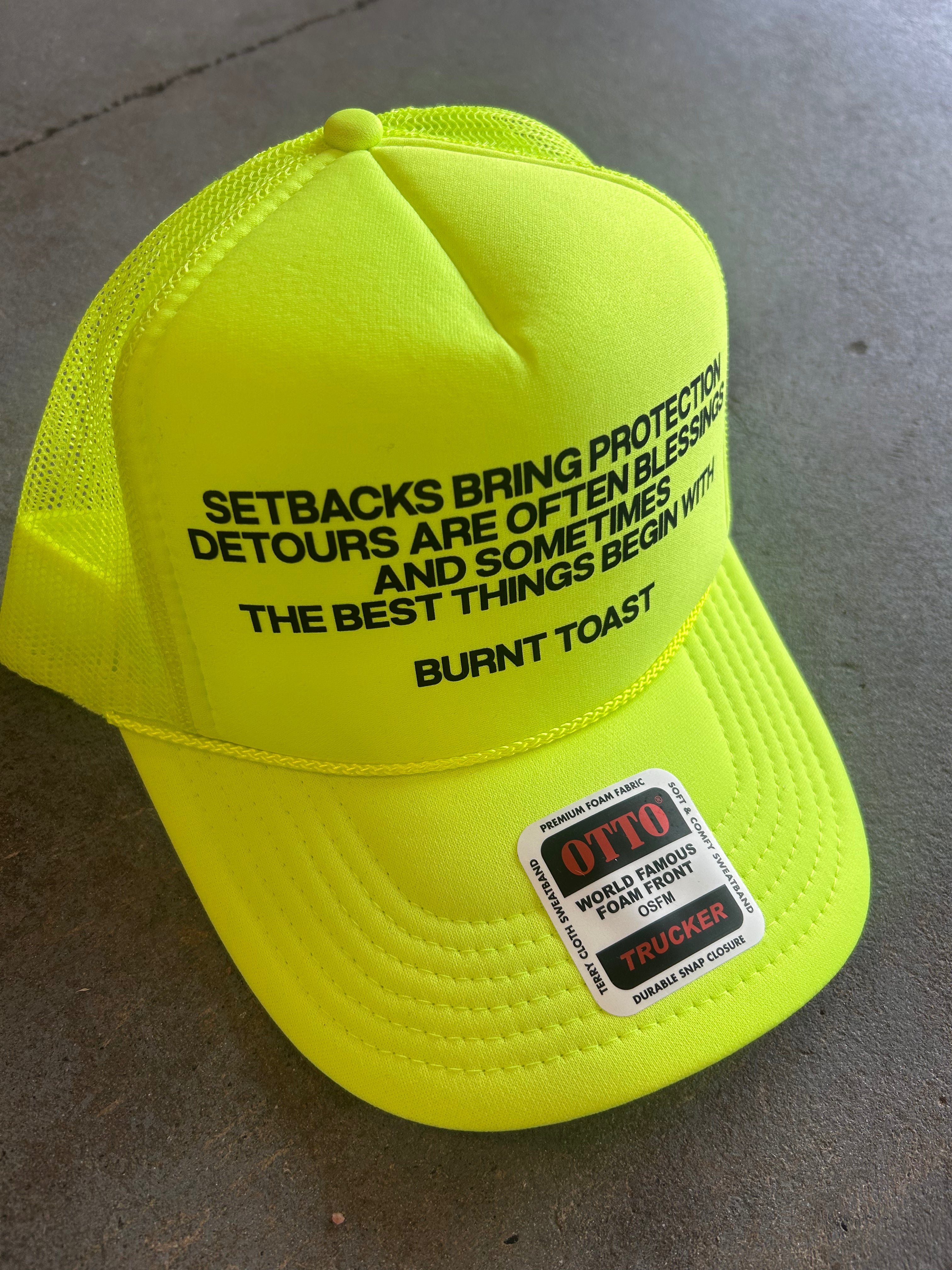 Neon Yellow Trucker Hat with the Burnt Toast theory explanation written in black on the hat, frontal view on a concrete surface