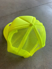 Back of a neon yellow mesh trucker hat on a concrete surface