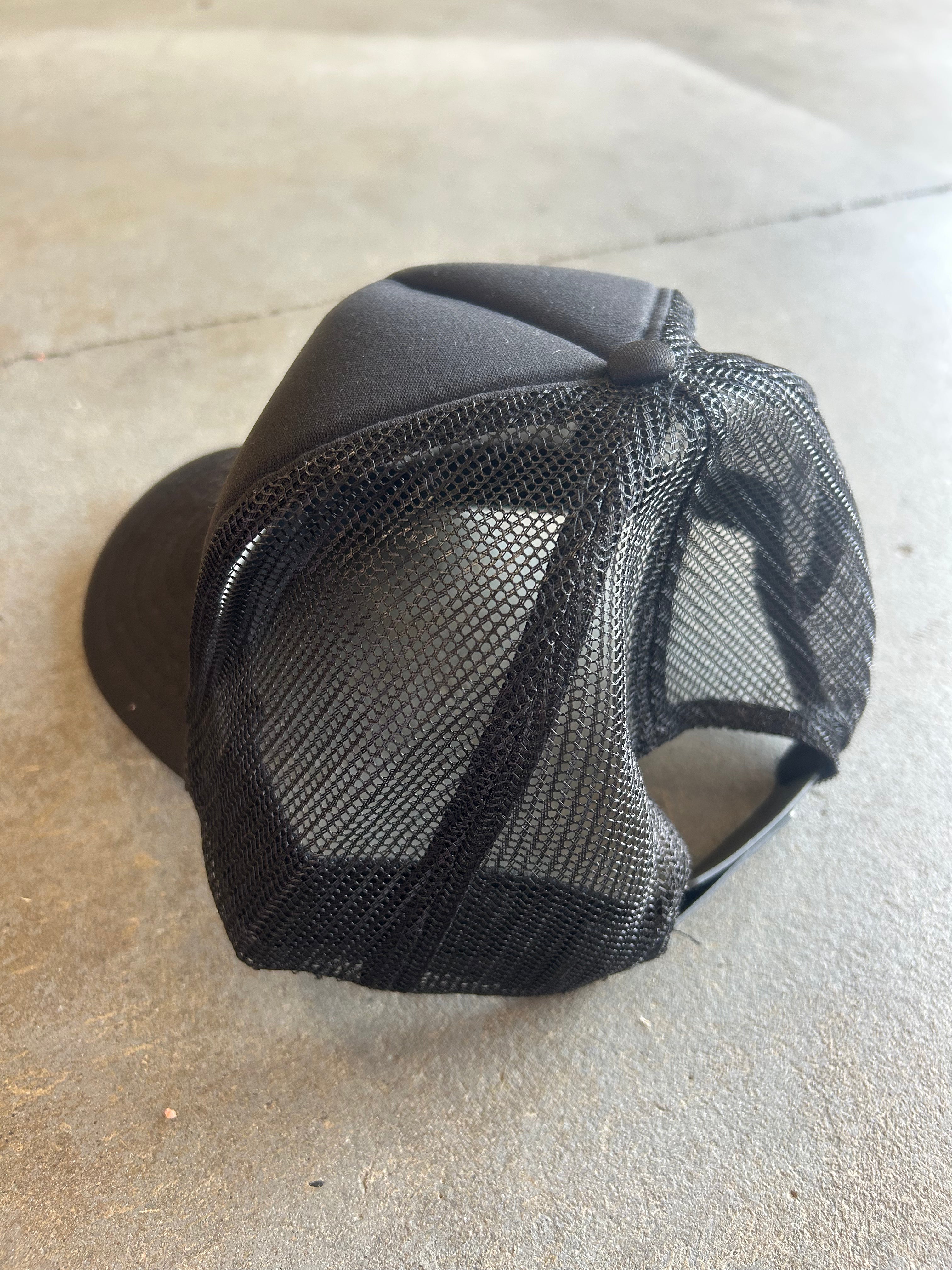 Back of black mesh trucker hat on a concrete surface