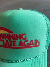 A mint green trucker hat with a red and yellow graphic on the front that reads 'RUNNING STATE AGAIN'