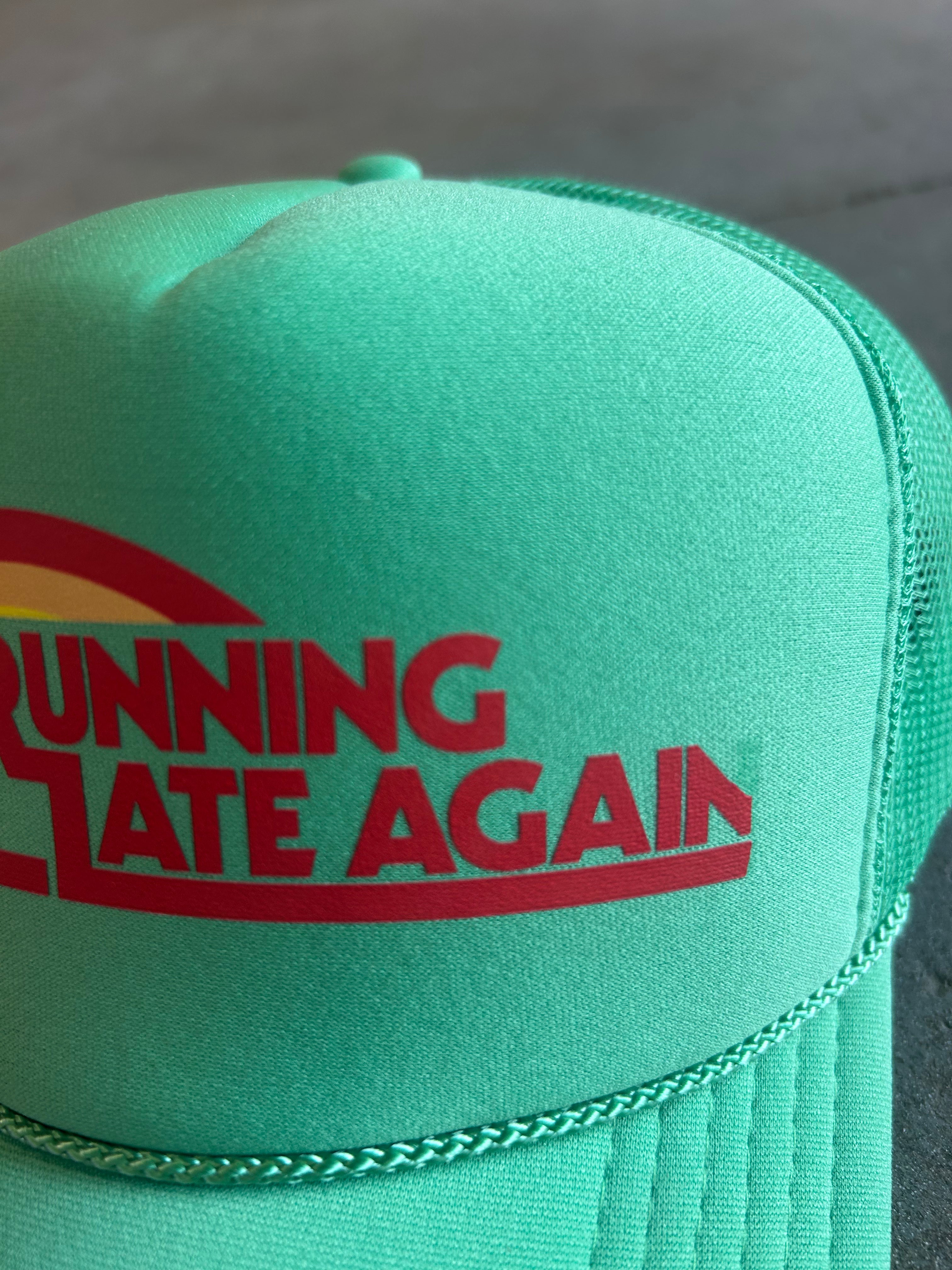 A mint green trucker hat with a red and yellow graphic on the front that reads 'RUNNING STATE AGAIN'