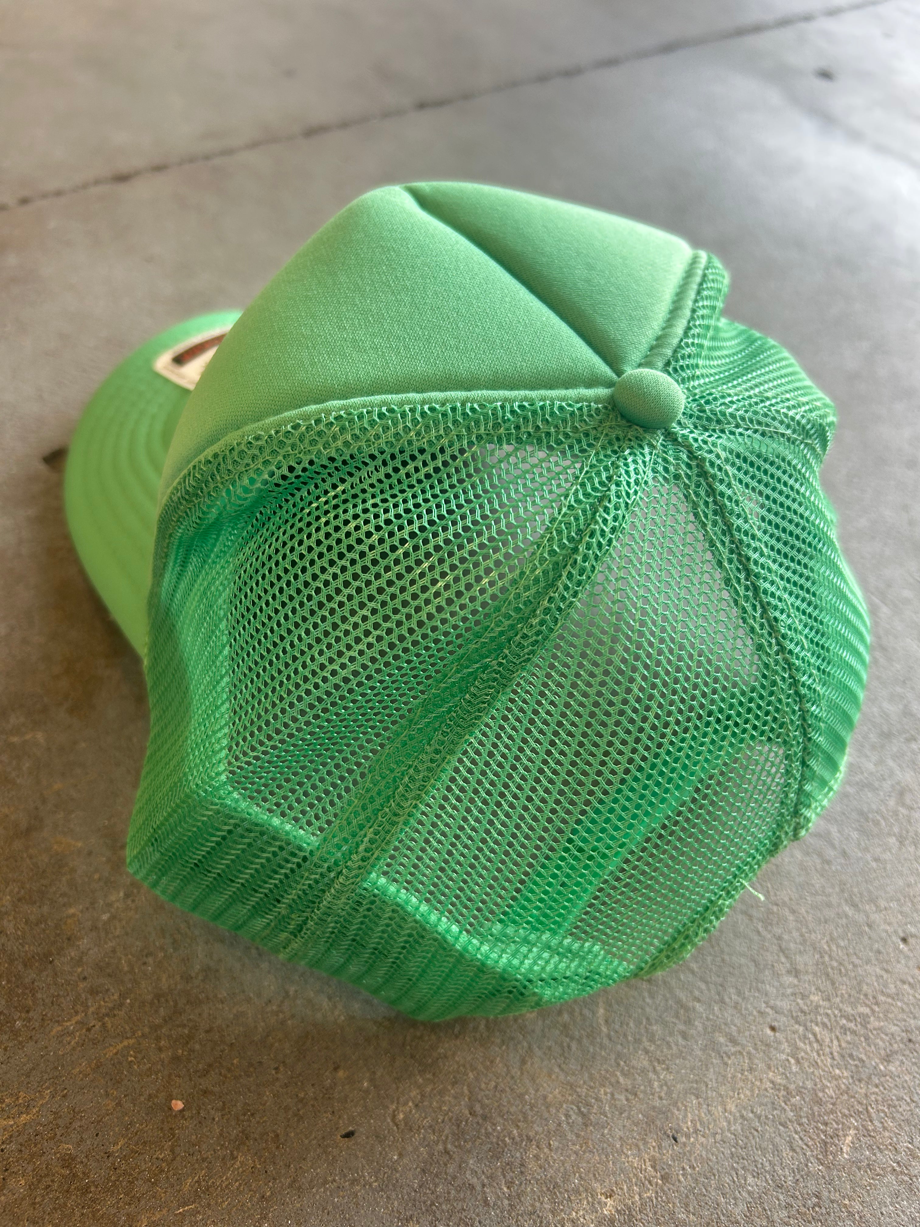 Back of a mint green mesh trucker hat on a concrete floor