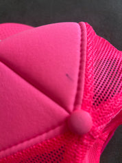 Close-up detail of a bright pink trucker cap showing the solid front fabric panel, mesh side panels, and matching pink snap button
