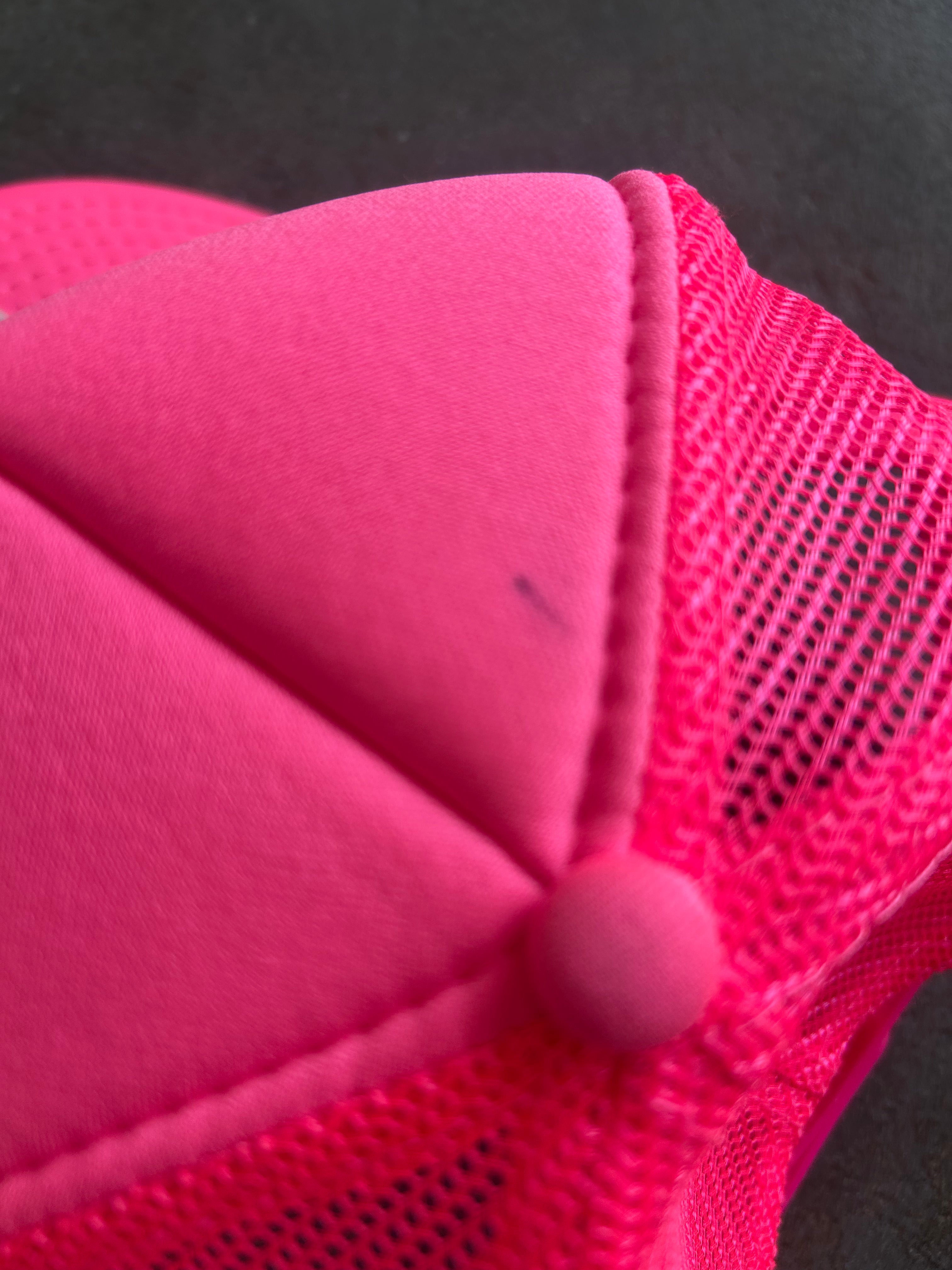 Close-up detail of a bright pink trucker cap showing the solid front fabric panel, mesh side panels, and matching pink snap button