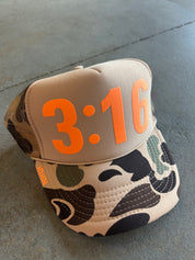 Tan trucker hat with camo accents on the brim and John 3:16 in neon orange on a concrete surface