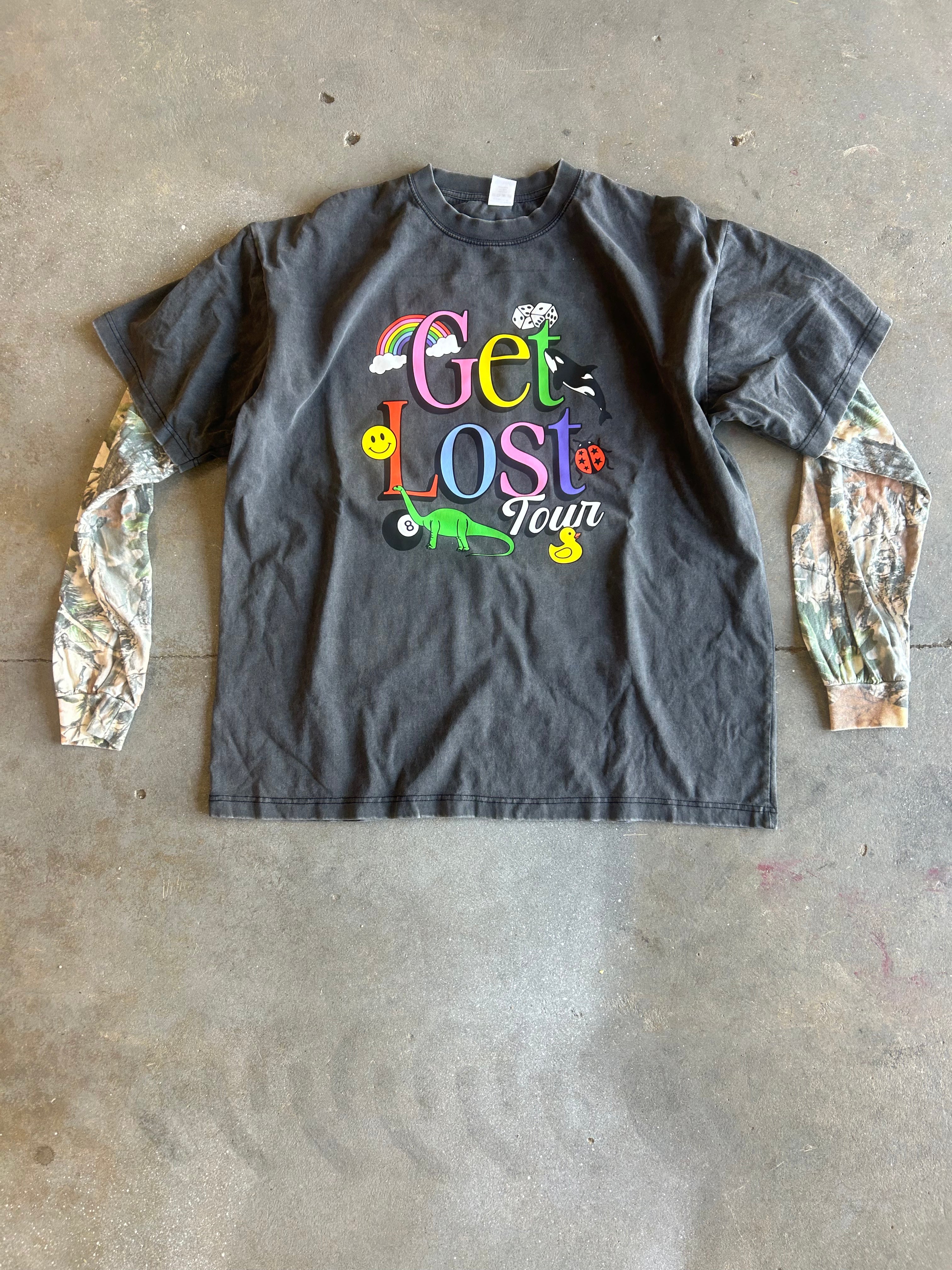 A dark gray graphic t-shirt with camouflage-print long sleeves, featuring a colorful 'Get Lost Your' graphic on the chest, laid flat on a concrete floor
