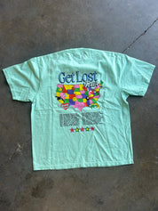 Back of a tee shirt with Get Lost and map of the US and text below on a concrete surface