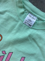 A close-up of a mint green t-shirt showing the inner collar label which reads 'SHAKA WEAR' and 'SUNRISE DYE', alongside a size marking of '3XL'.