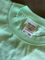 Close-up of a mint green t-shirt collar showing the inner neck label which reads 'SHAKA WEAR' and 'GARMENT DYE 3XL'.