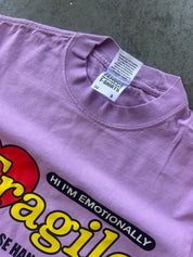 A close-up of a lavender purple t-shirt showing the inner collar with a white Shaka brand tag and part of a colorful graphic print featuring yellow text and a red heart.