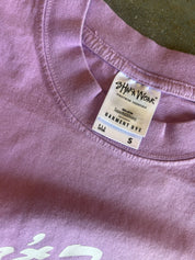 Close-up of a lavender-purple t-shirt showing the inner collar with a white 'Shaka Wear' garment dye tag.