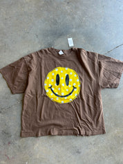 Brown tee with a yellow smiley face graphic on a conrete surface