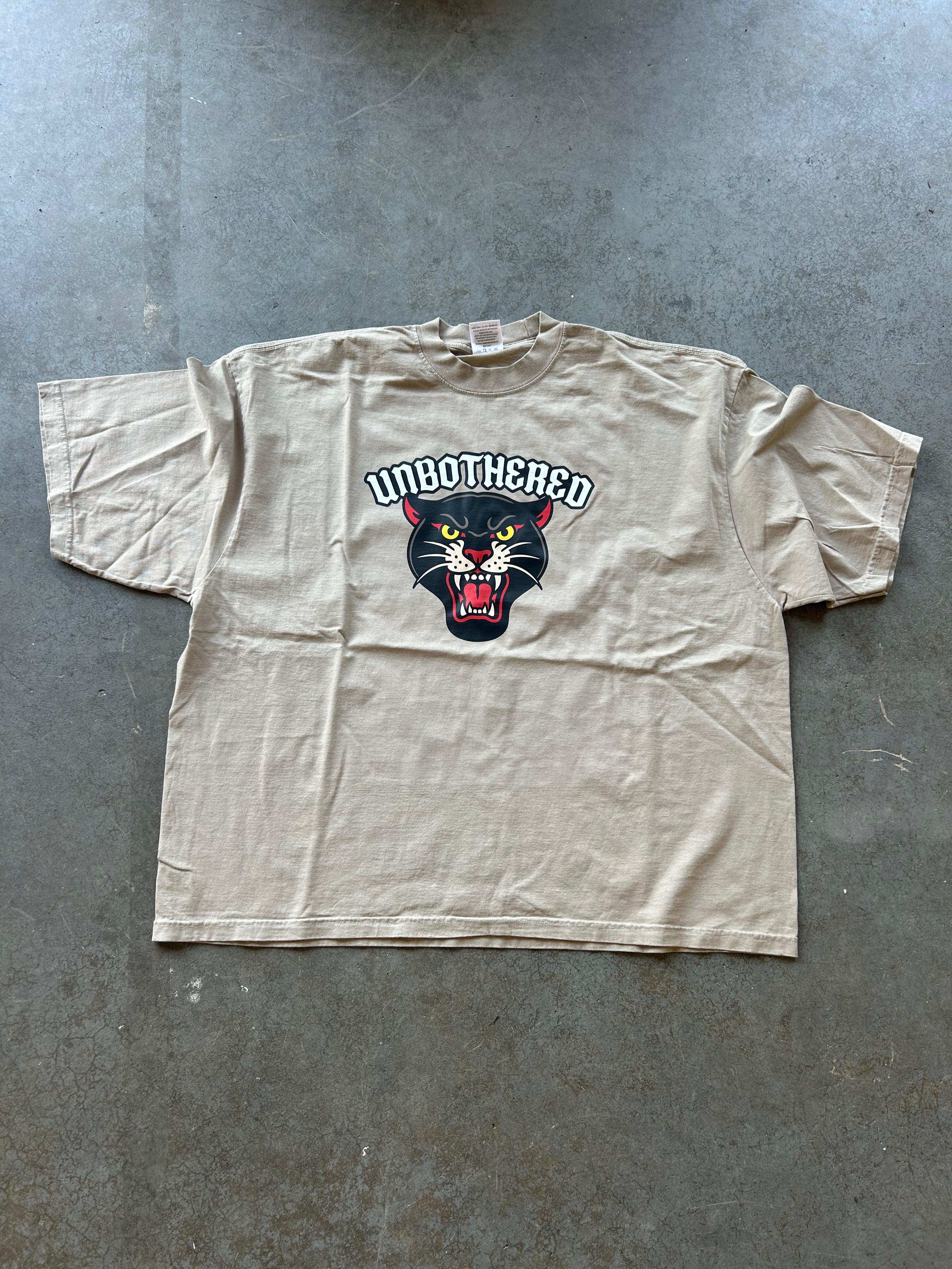 Oatmeal t shirt with Unbothered text and panther on a concrete surface