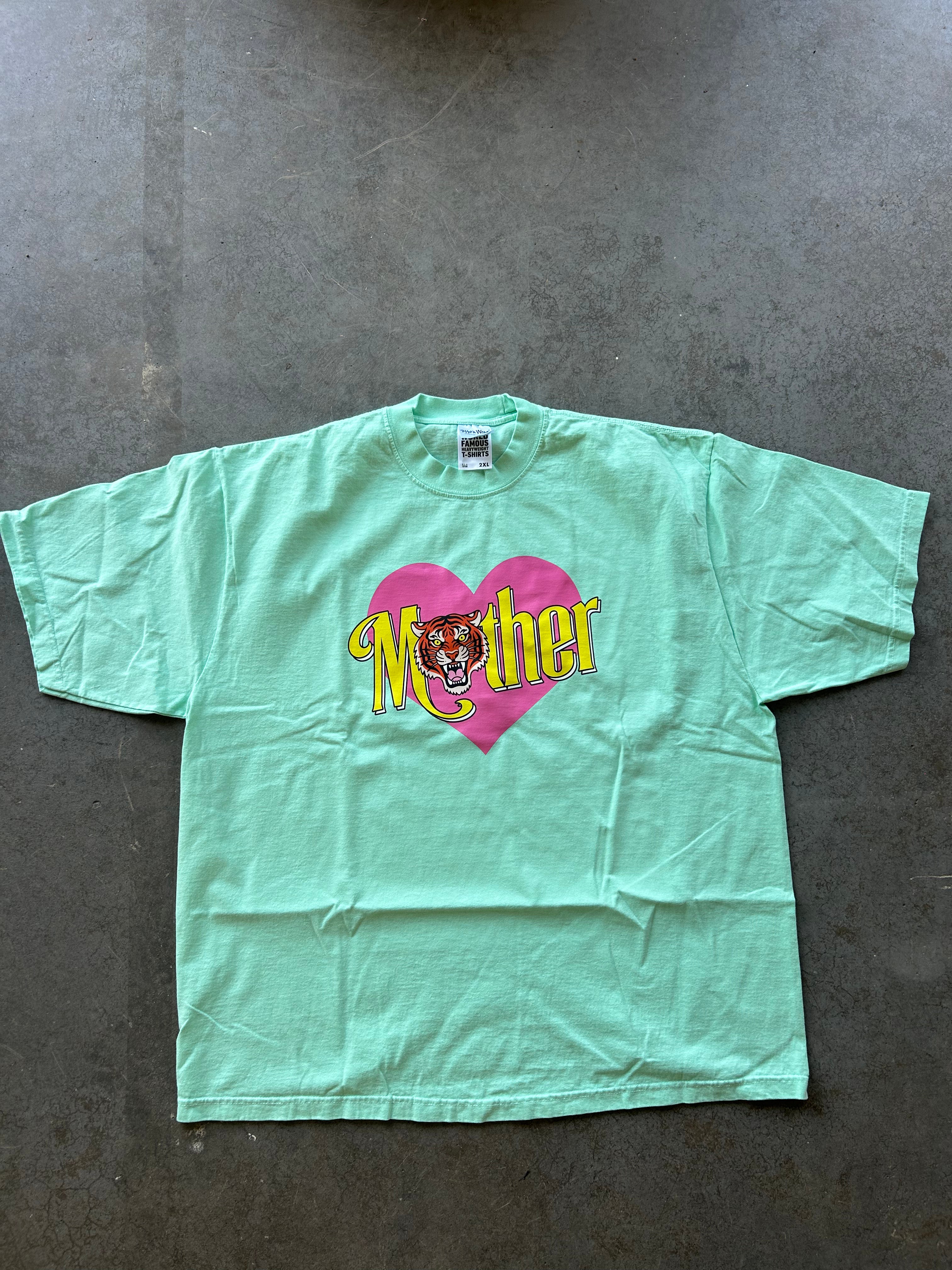 Seafoam green tee with a pink heart and Mother text on a concrete surface