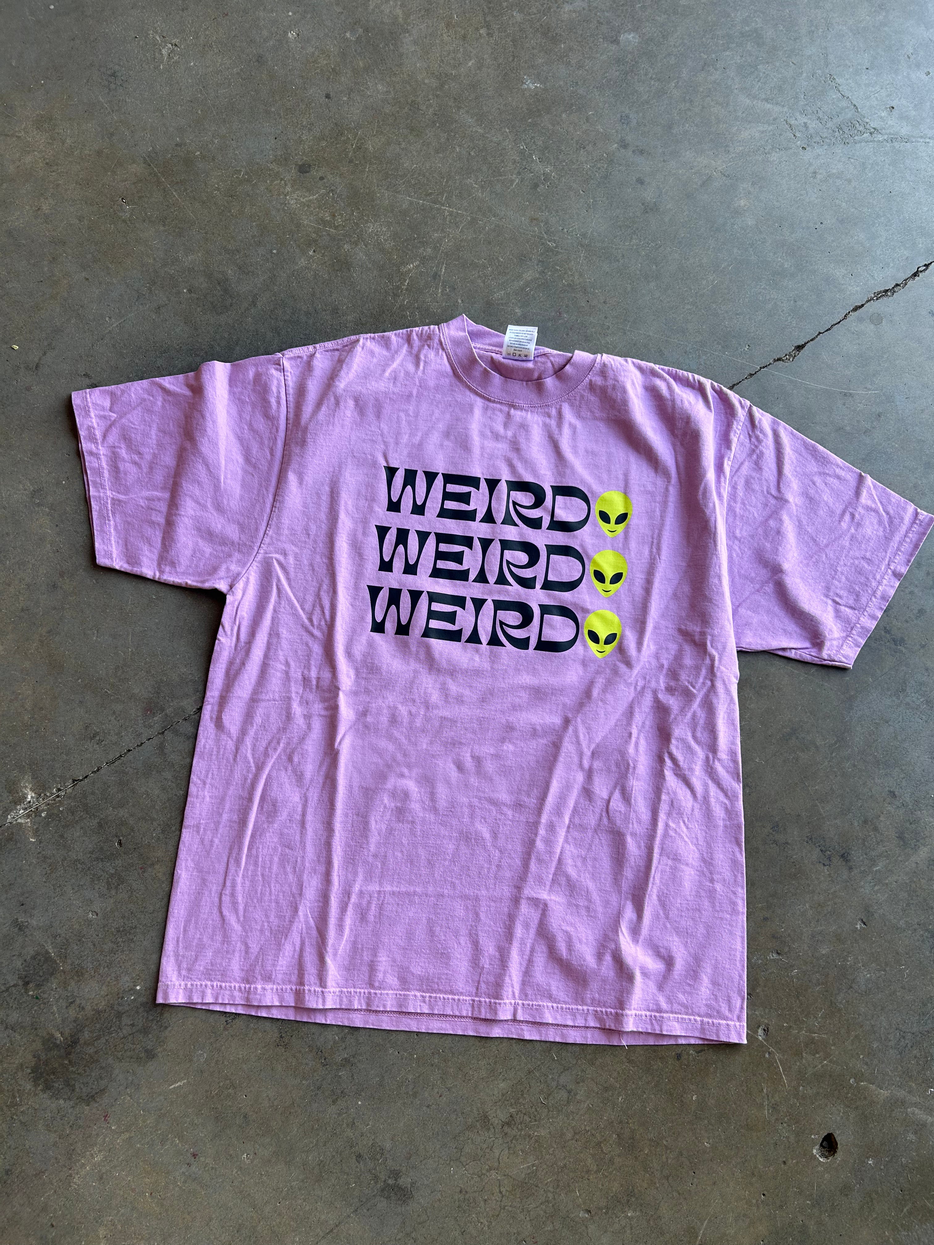 Weirdo x3 graphic on a purple shirt on a concrete floor