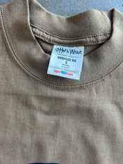Close-up of an oversized crewneck t-shirt in a muted taupe-brown color, showing the inner neck label for 'Sha'a Wear'.