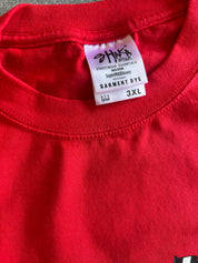 Close-up of a bright red crewneck t-shirt showing the inner neck label which reads 'STRIKE A WORK STREETWEAR ESSENTIALS' and 'GARMENT DYE 3XL'.