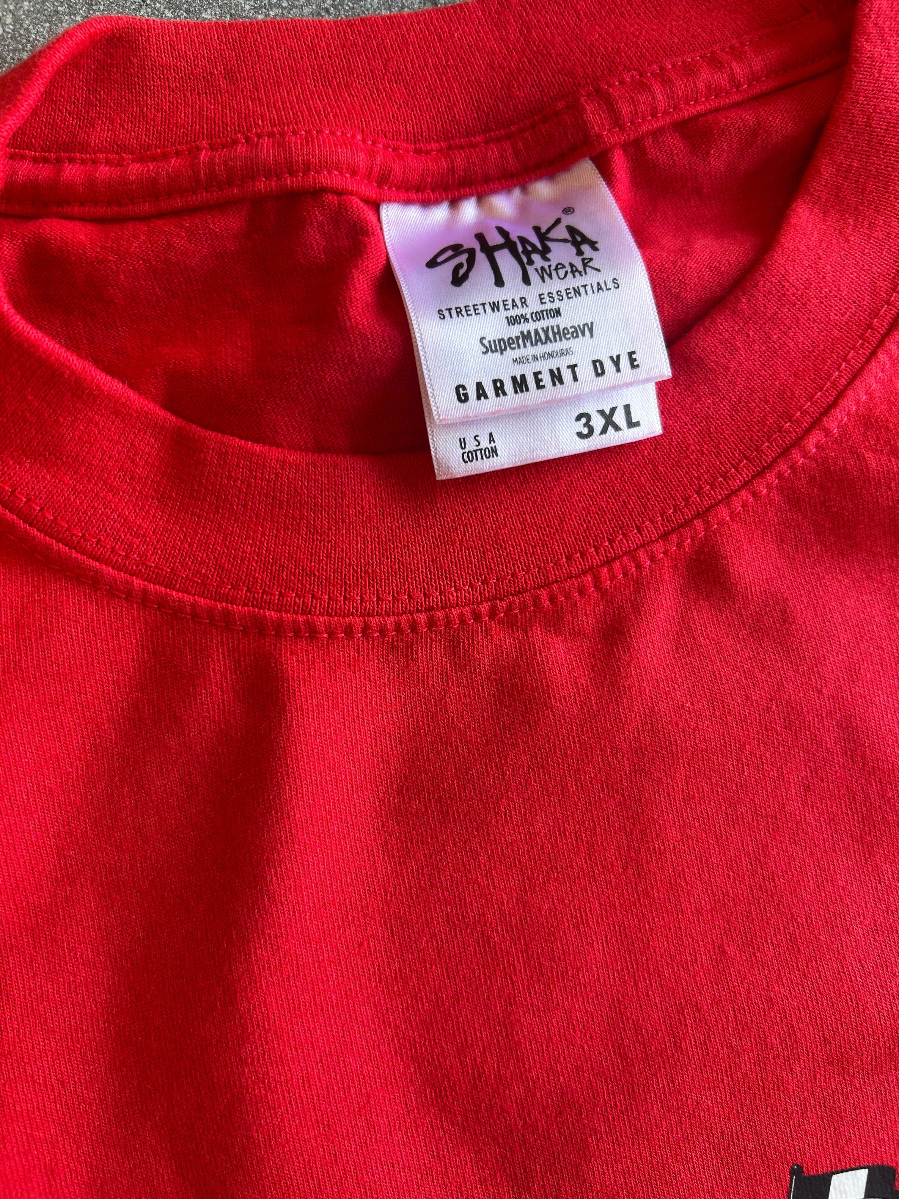 Close-up of a bright red crewneck t-shirt showing the inner neck label which reads 'STRIKE A WORK STREETWEAR ESSENTIALS' and 'GARMENT DYE 3XL'.