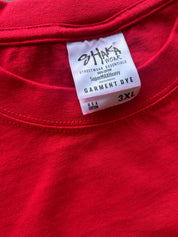 Close-up of a red garment dye label on a red t-shirt collar, showing the brand 'SHAKA WORK' and size '3XL'.