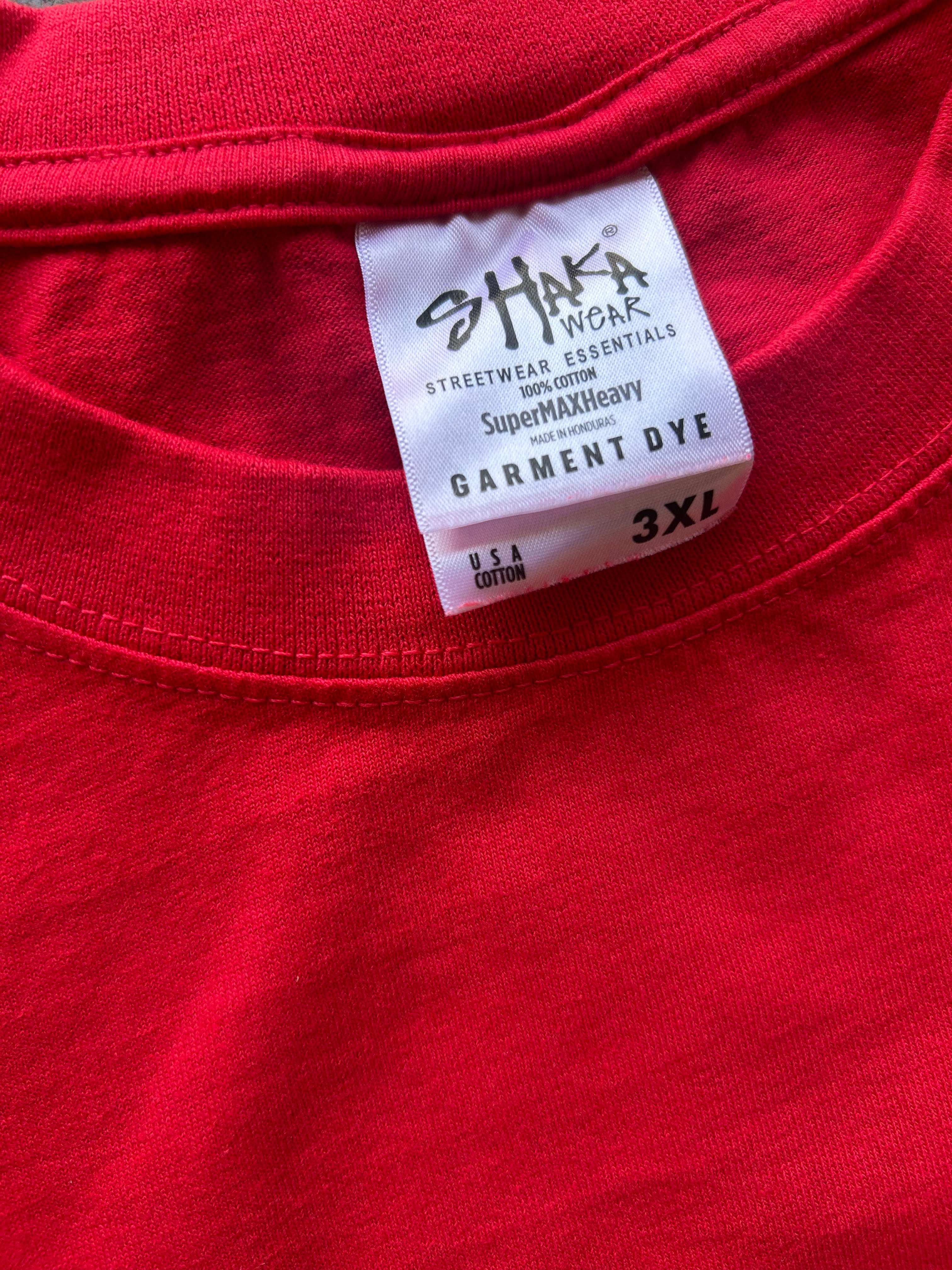 Close-up of a red garment dye label on a red t-shirt collar, showing the brand 'SHAKA WORK' and size '3XL'.