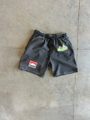 Black athletic shorts with an elastic waistband, featuring a red and white 'Torsion' patch on the left leg and a green and white 'Buckeye' patch on the right leg, laid flat on a concrete floor