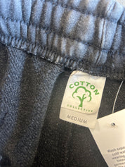 Close-up of a gray heathered fabric garment with a sewn-on label reading COTTON COLLECTIVE and MEDIUM, plus a white care tag attached