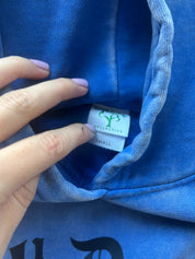 Close-up of a blue hoodie interior showing a hand pointing to the inner neck label which reads 'COLLECTIVE' and 'SMALL'.