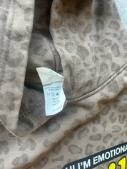 Close-up of a leopard print garment, likely a sweatshirt or hoodie, showing the interior neck area with a white size tag labeled XLARGE. The fabric has a beige and gray animal print pattern.