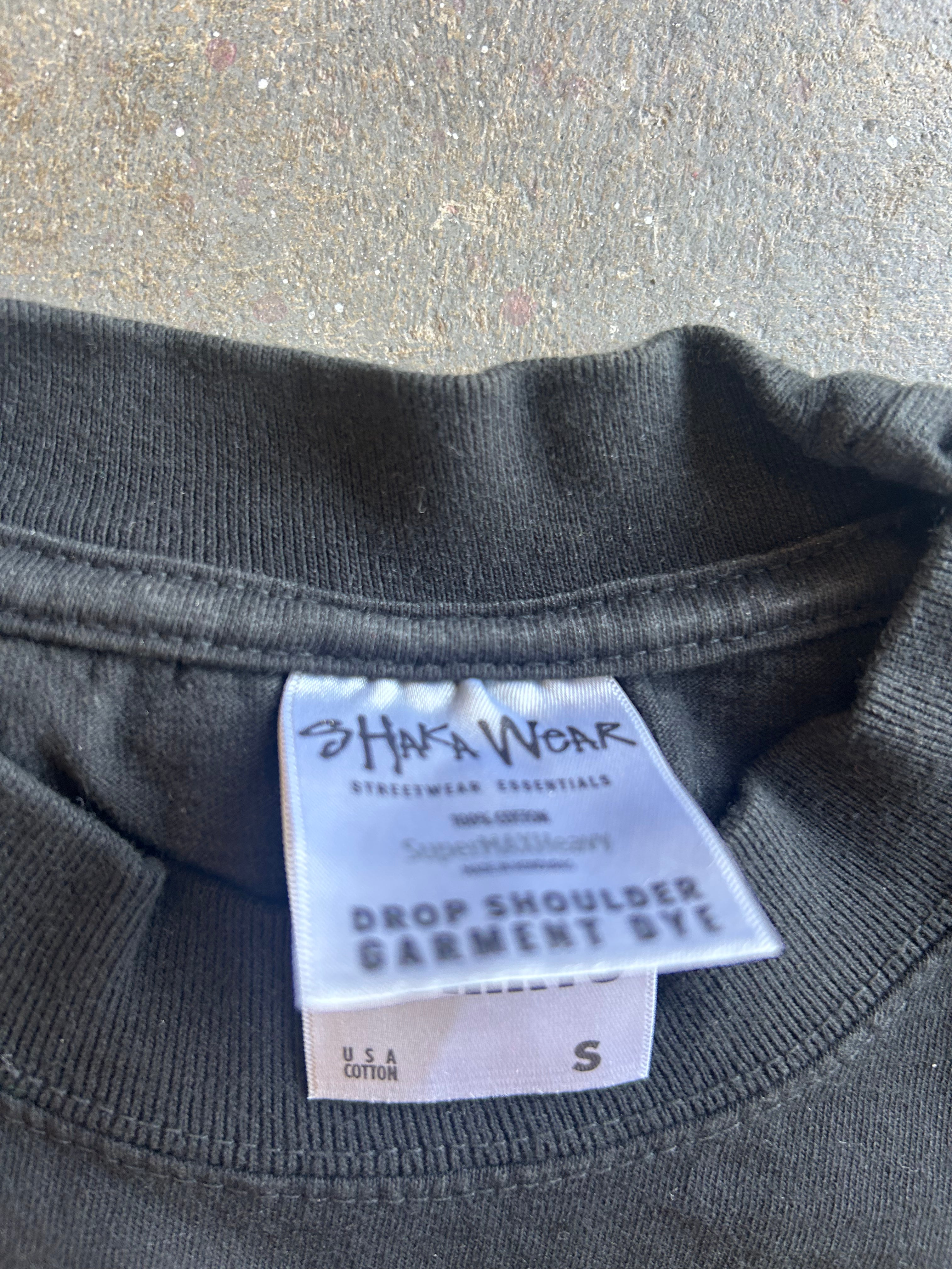 Close-up of the inside neck of a dark charcoal gray garment dyed sweatshirt, showing a white paper label that reads 'Hafa Wear' and 'Drop Shoulder Garment Dye'.