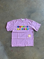 Purple tee with School is Cool text in candy hearts, flat lay on a concrete surface