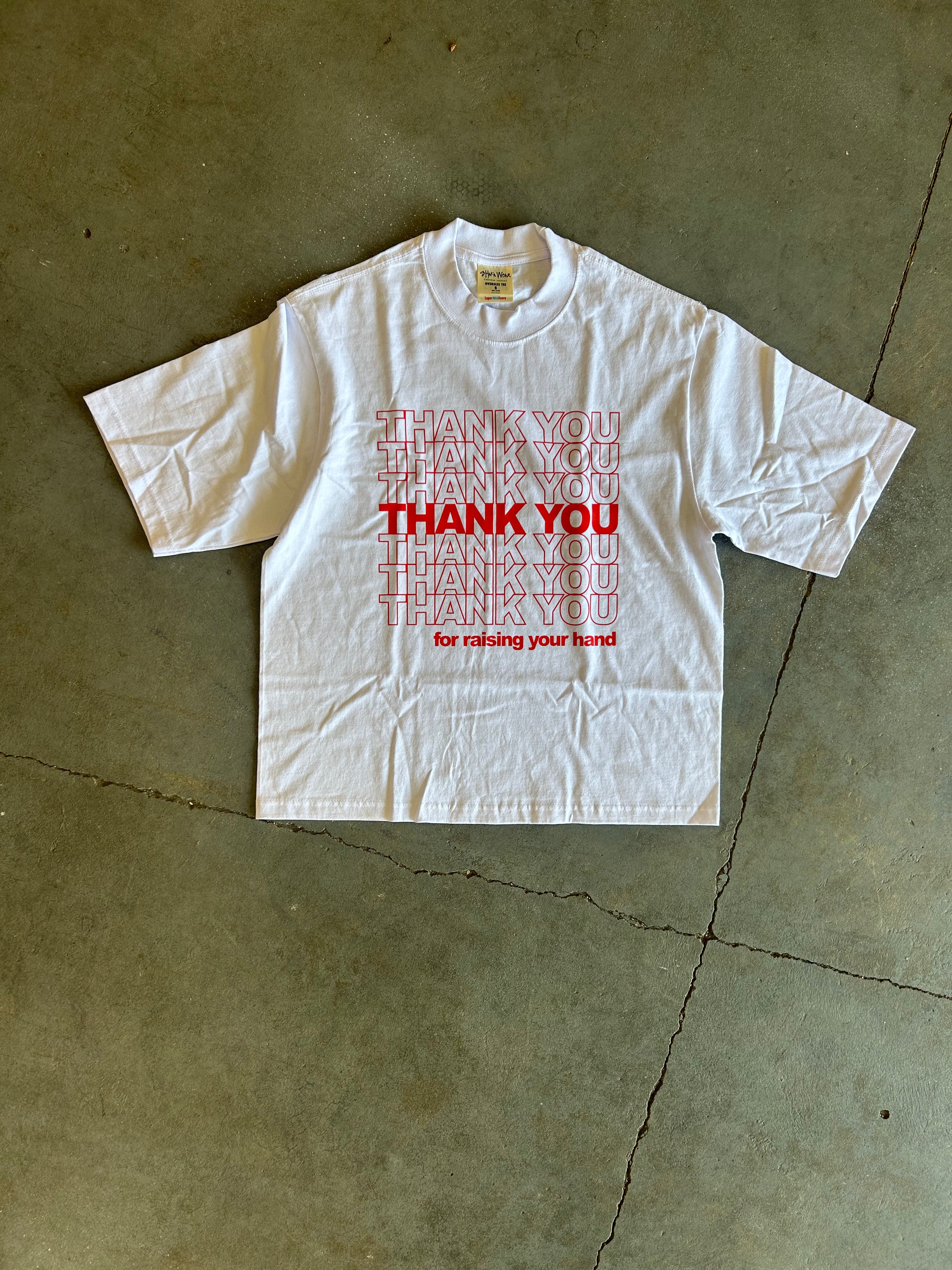 A white short-sleeve T-shirt laid flat on a concrete floor, featuring a red graphic print that reads 'THANK YOU for raising your funds' with repeated 'THANK YOU' text in red and pink.