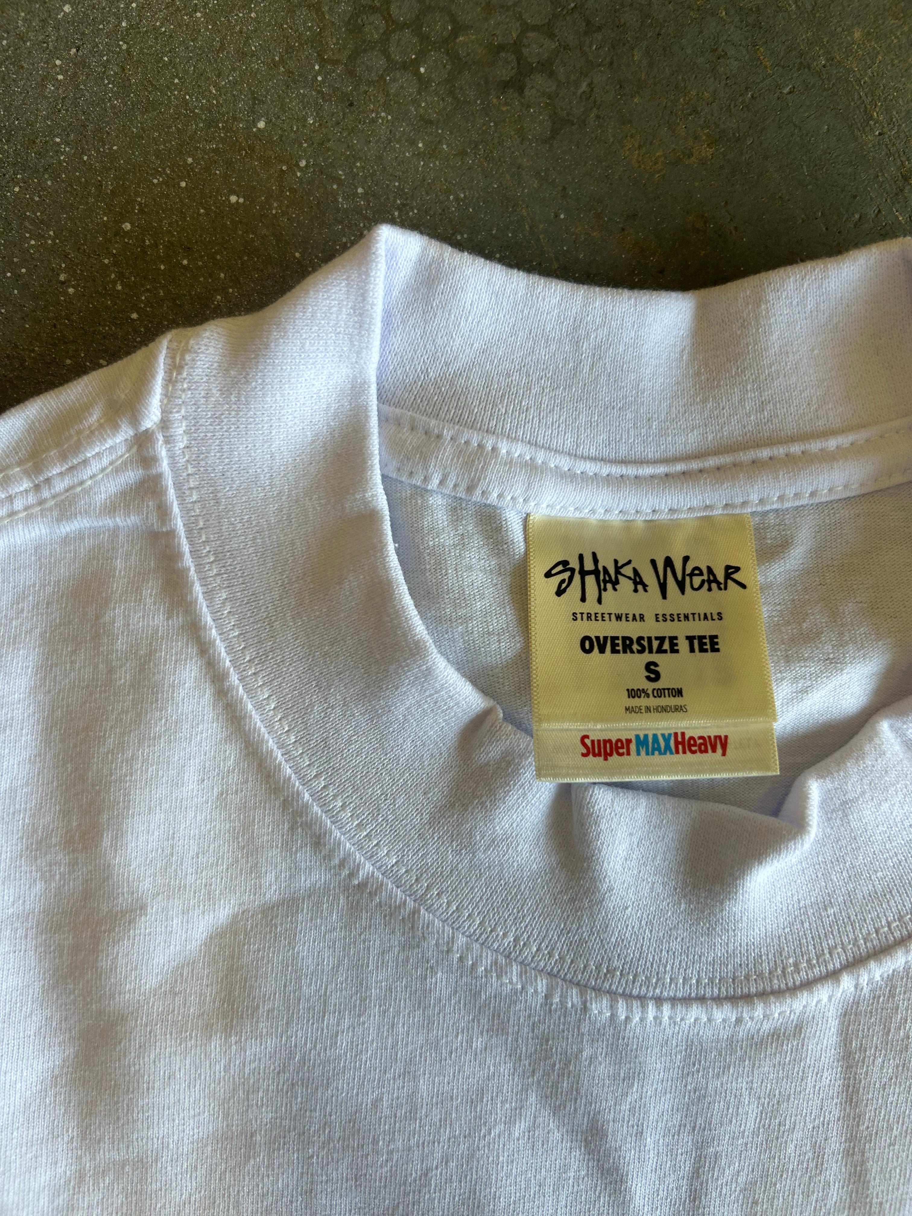 Close-up of a white oversized crewneck t-shirt collar showing the inner neck label which reads 'SHAKA WEAR' and 'OVERSIZE TEE S'.
