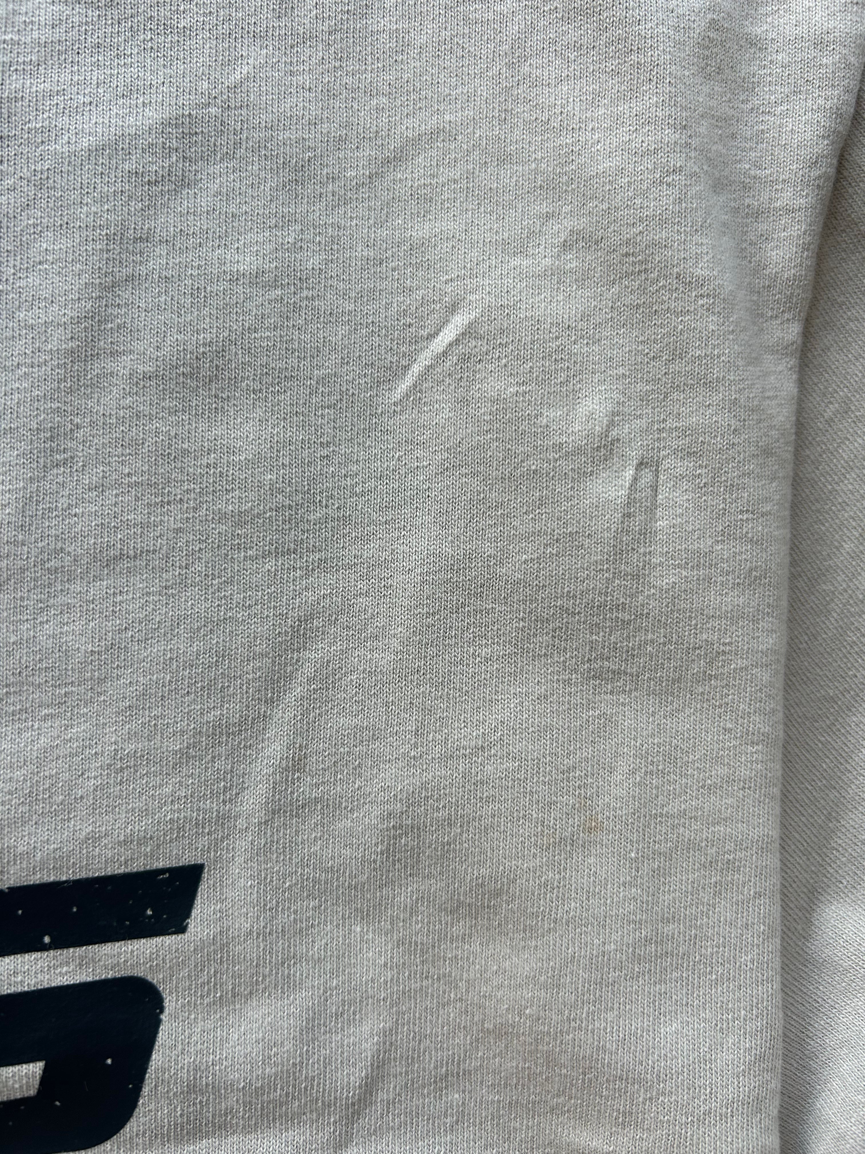 Close-up of a light gray heather fabric surface with a small black graphic fragment visible at the bottom left and a few minor scuffs or marks on the material.