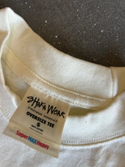 Close-up of the inside collar of an oversized off-white cotton t-shirt, showing a white brand label that reads 'SHAKA WEAR' and 'Super MAX Heavy'.