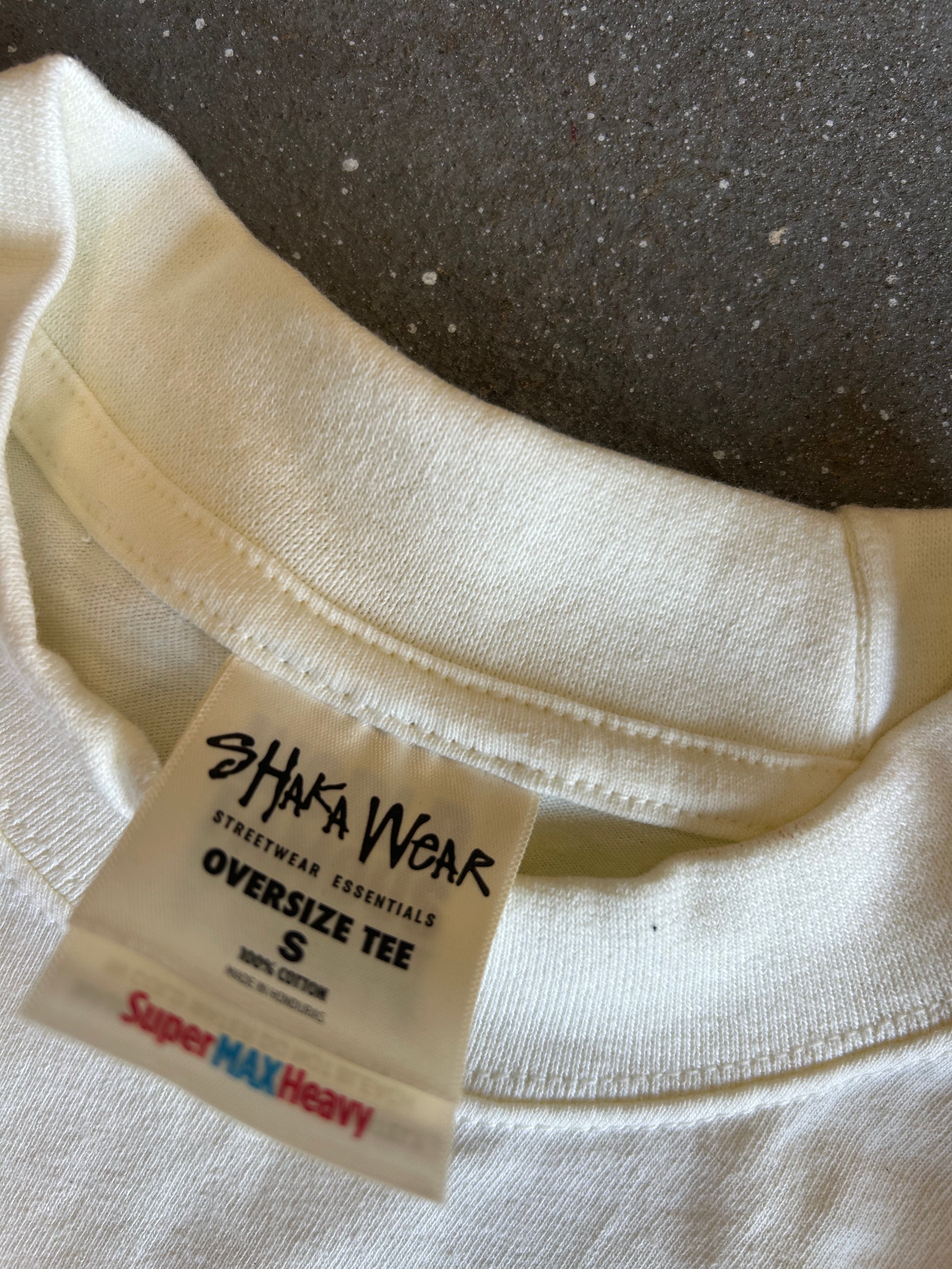 Close-up of the inside collar of an oversized off-white cotton t-shirt, showing a white brand label that reads 'SHAKA WEAR' and 'Super MAX Heavy'.