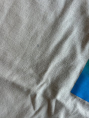 A close-up of light gray fabric with visible texture and soft folds, with a small blue area visible in the lower-right corner.