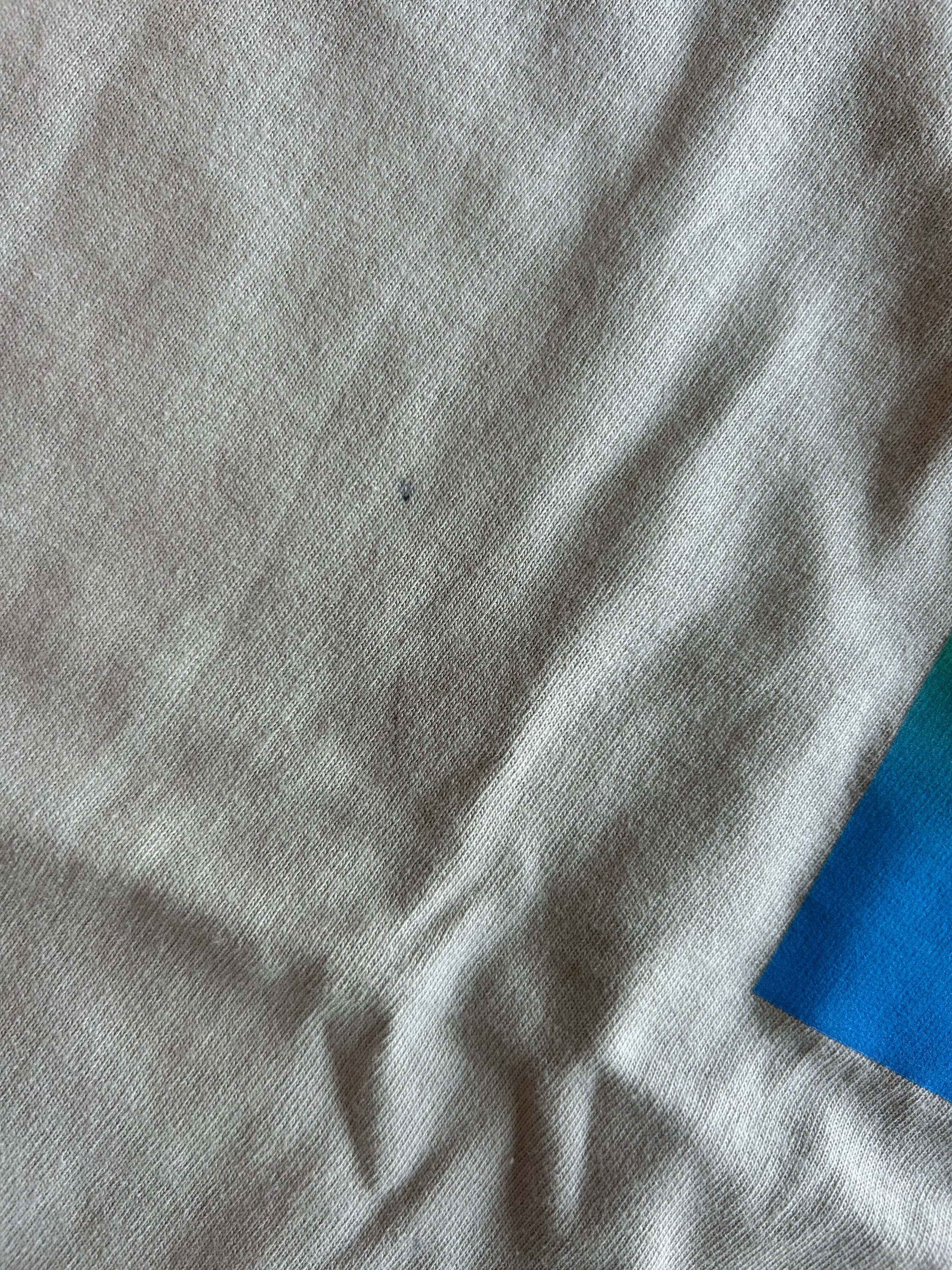 A close-up of light gray fabric with visible texture and soft folds, with a small blue area visible in the lower-right corner.