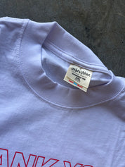 Close-up of a light lavender crewneck t-shirt with a visible '24/7 Wear' brand tag, laid flat on a textured gray surface.